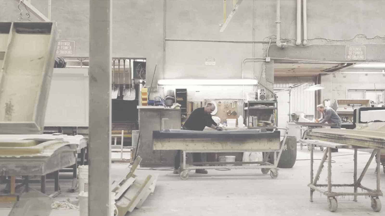 Atelier industriel avec deux personnes travaillant sur des tables de travail sur roulettes et divers matériaux et outils autour