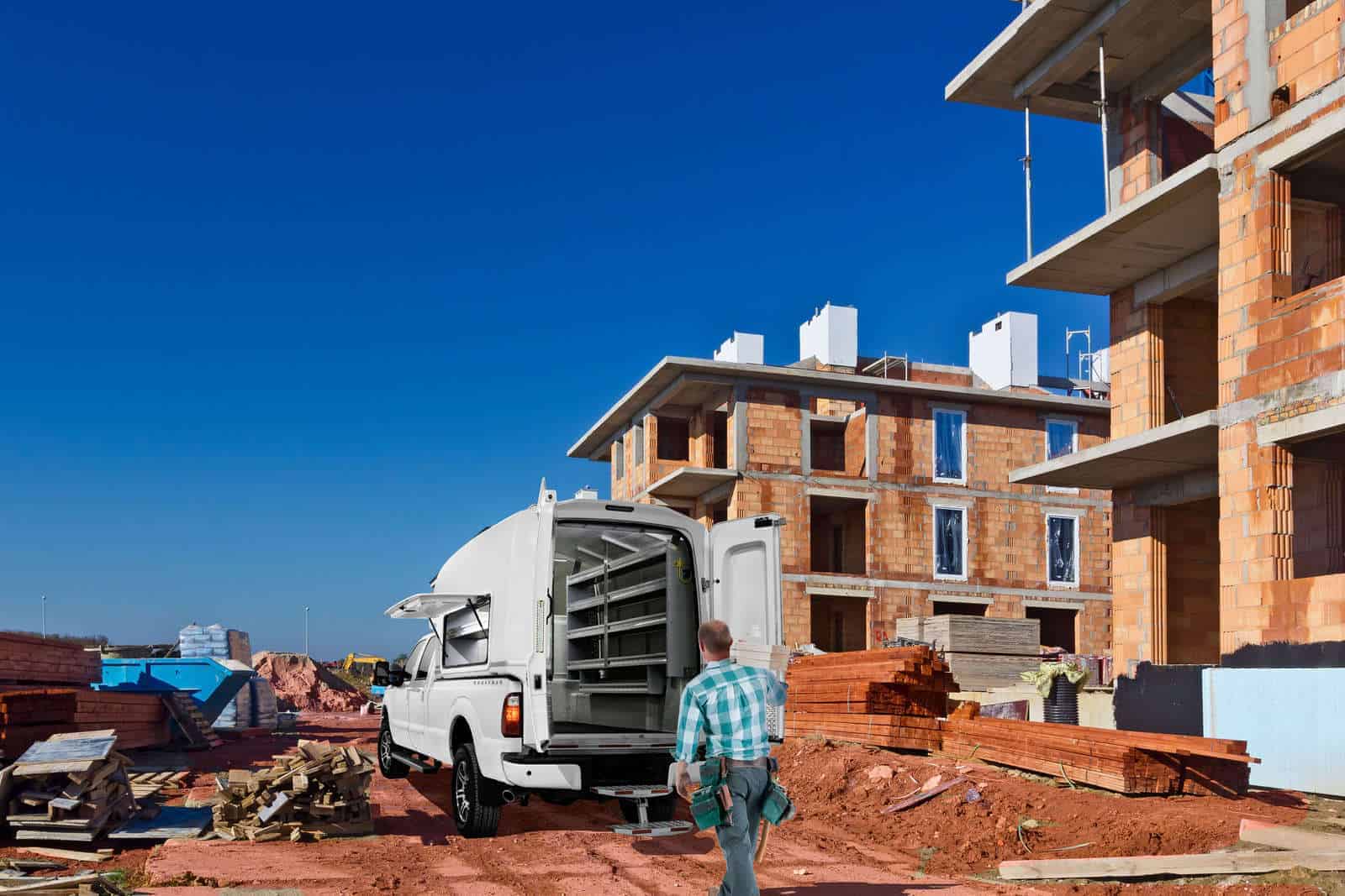 Man approaching white truck with open storage box at construction site with unfinished buildings