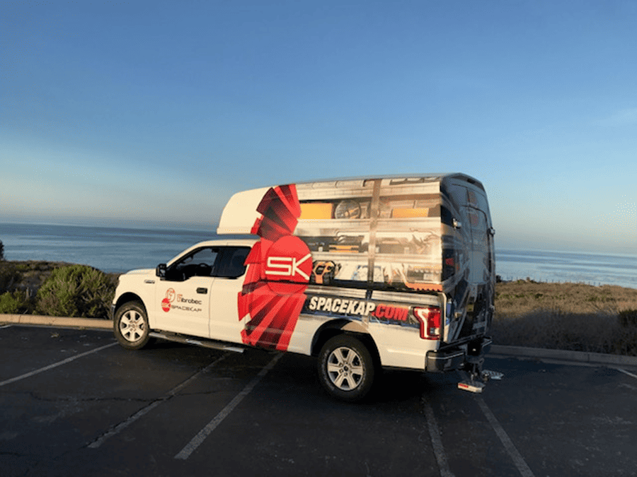 Camionnette blanche avec un auvent SpaceKap stationnée face à l'océan sous un ciel clair