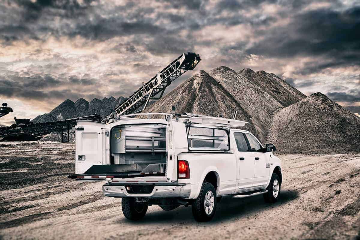 Camionnette blanche équipée pour le travail sur un site de construction avec des tas de matériaux et un ciel nuageux