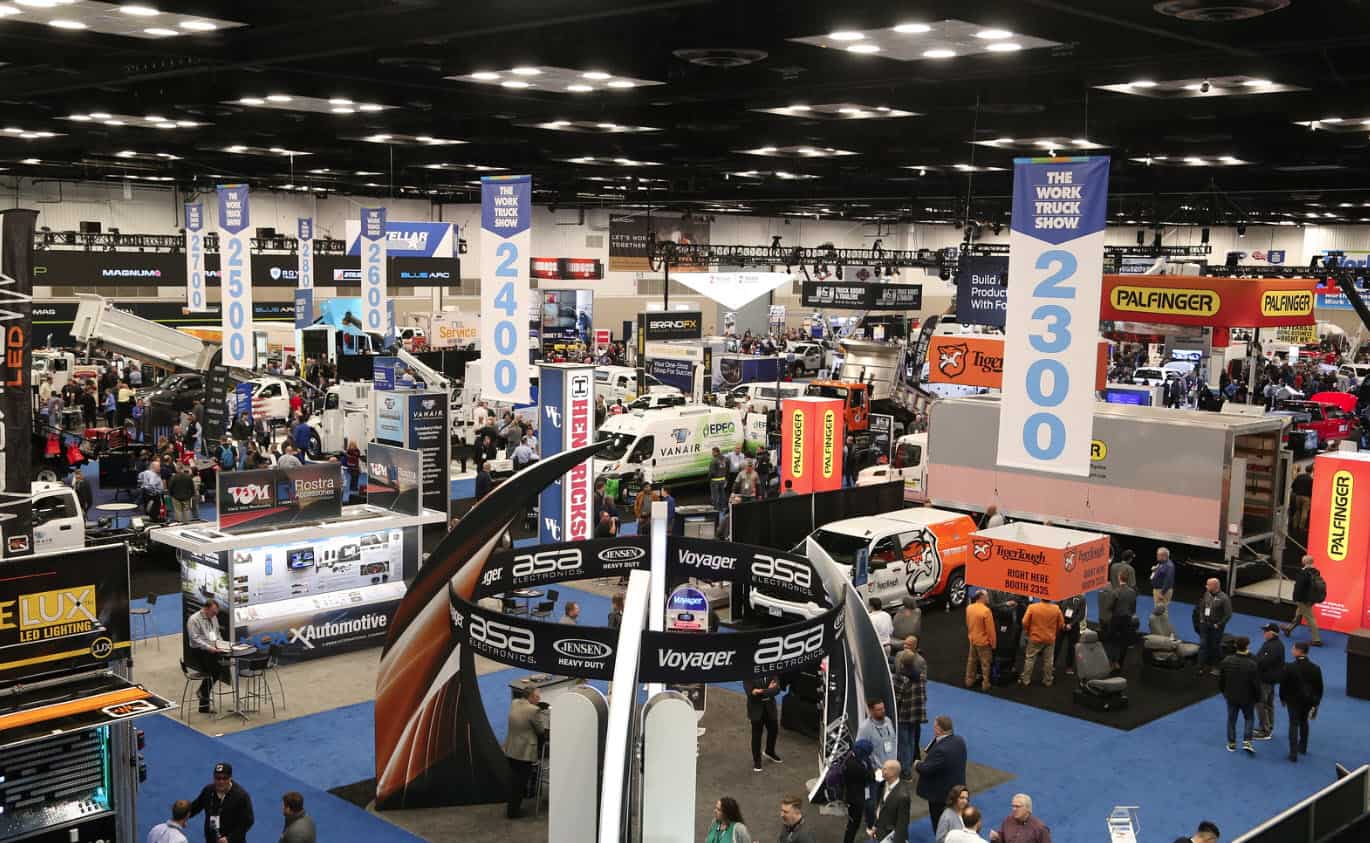 Vue panoramique d'un salon professionnel dédié aux camions et équipements de travail avec plusieurs stands et véhicules exposés