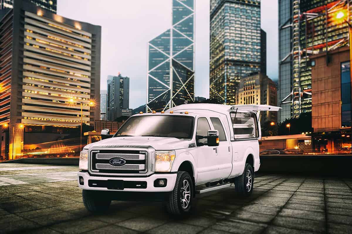 Camion Ford blanc stationné dans une ville la nuit avec des gratte-ciels illuminés en arrière-plan