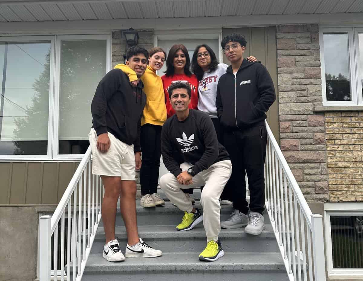 Groupe de six jeunes souriants posant sur les marches d'une maison résidentielle moderne avec des vêtements décontractés colorés.