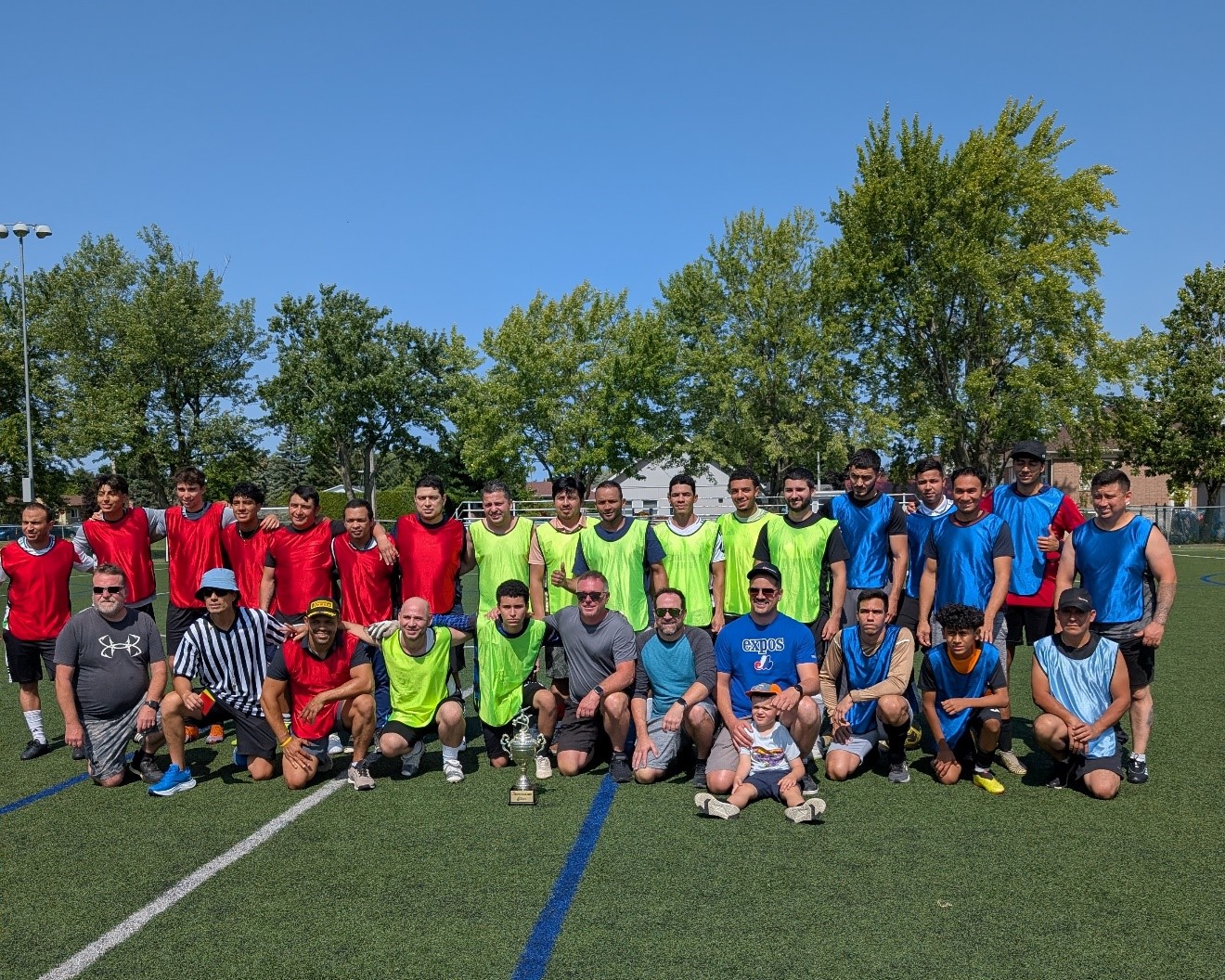 Photo d'un grand groupe d'hommes portant des chandails de différentes couleurs sur un terrain de soccer extérieur par jour ensoleillé