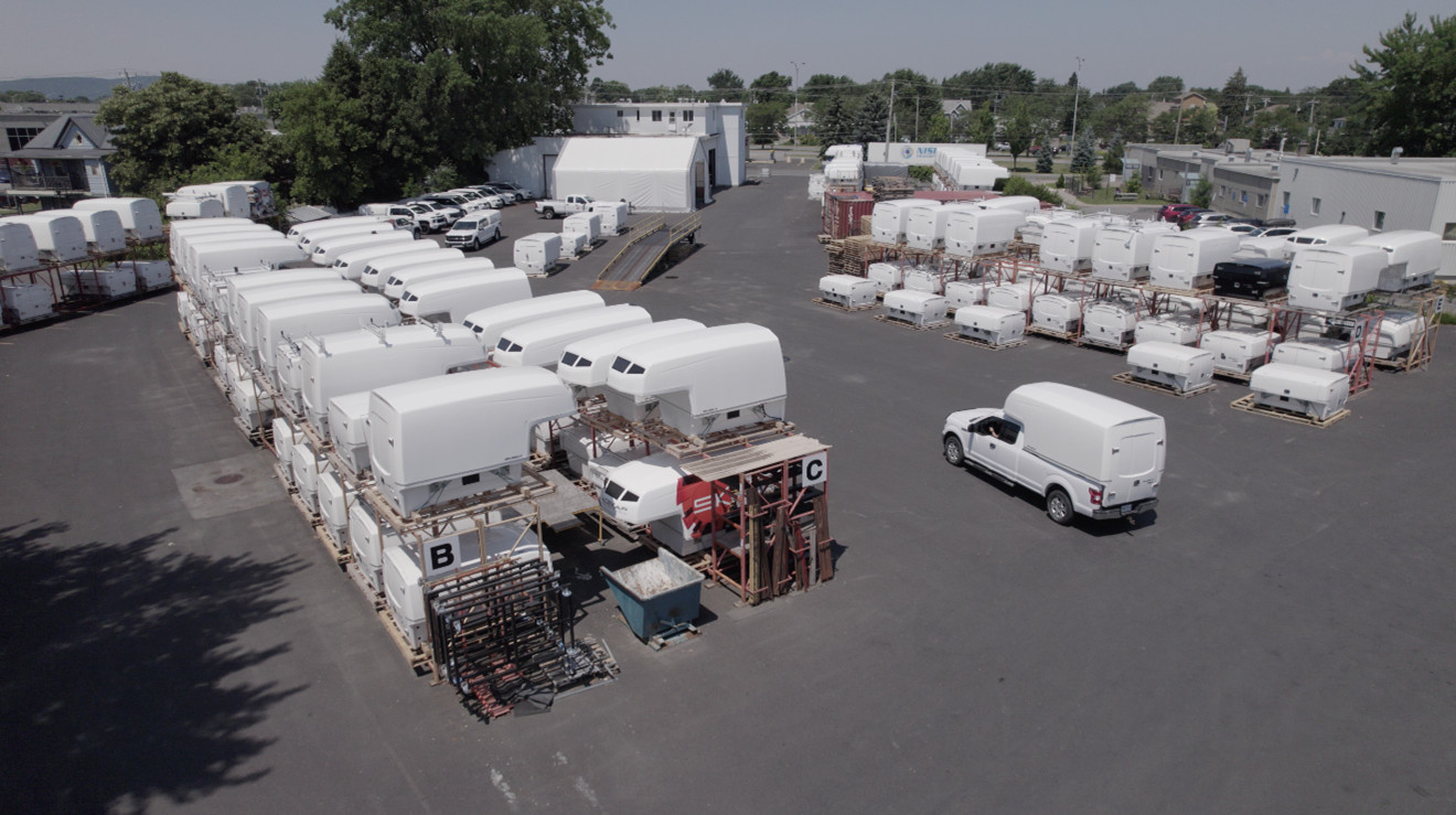 Vue aérienne d'une cour industrielle avec plusieurs coffres de remorque blancs empilés et un camion blanc en mouvement