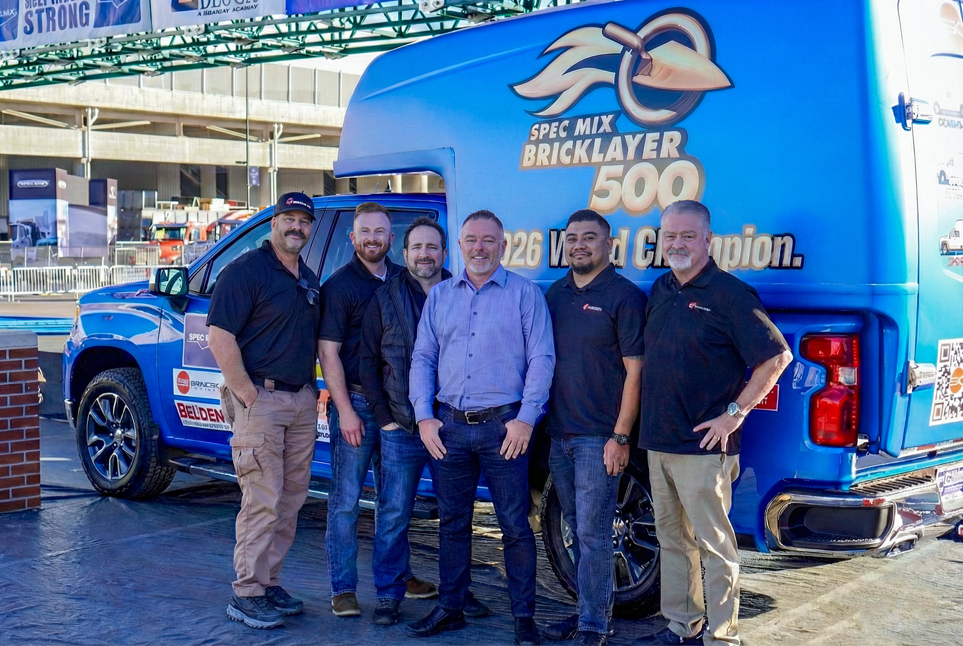 Group of six men standing in front of a blue truck with Spec Mix Bricklayer 500 logo