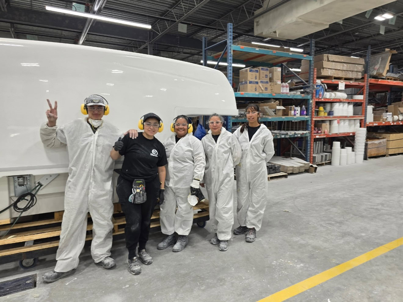 Cinq travailleurs portant des combinaisons blanches et équipements de protection posent dans un atelier industriel devant une grande boîte en fibre de verre.